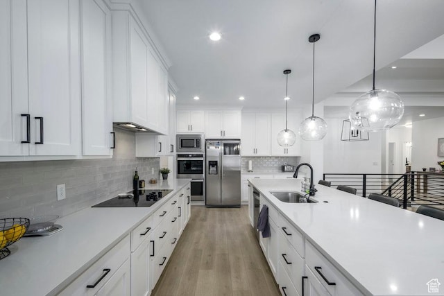 kitchen featuring light countertops, light wood-style flooring, white cabinets, stainless steel appliances, and a sink