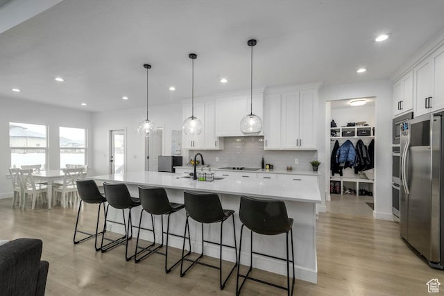 kitchen with light countertops, decorative backsplash, appliances with stainless steel finishes, white cabinets, and a sink