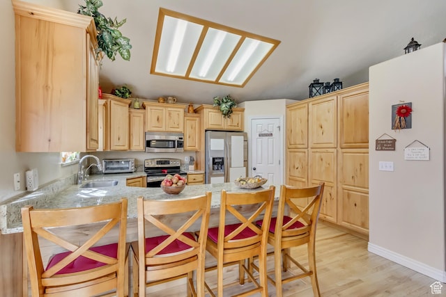 kitchen with light brown cabinets, a peninsula, stainless steel appliances, light wood-type flooring, and vaulted ceiling with skylight