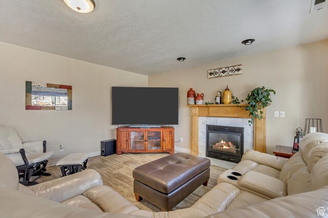 living room with a tile fireplace, a textured ceiling, baseboards, visible vents, and light wood-style floors