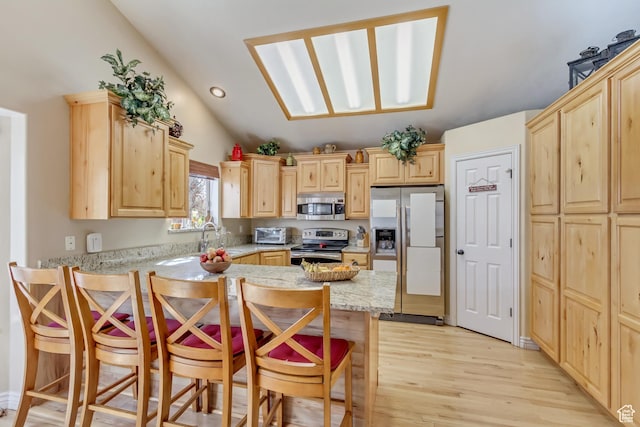 kitchen featuring stainless steel appliances, a breakfast bar, vaulted ceiling, light wood finished floors, and light brown cabinets