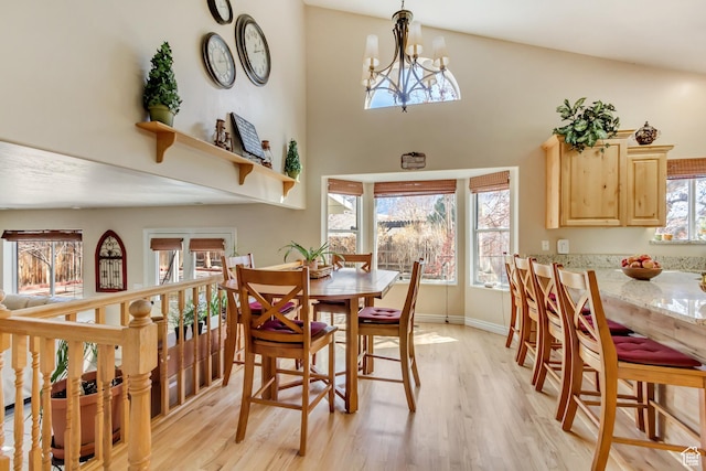 dining room featuring baseboards, a chandelier, light wood-type flooring, and a high ceiling