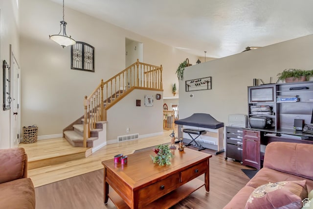 living room featuring light wood-style flooring, baseboards, visible vents, stairs, and high vaulted ceiling