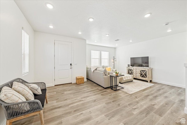 living area with recessed lighting, light wood-style floors, baseboards, and a textured ceiling