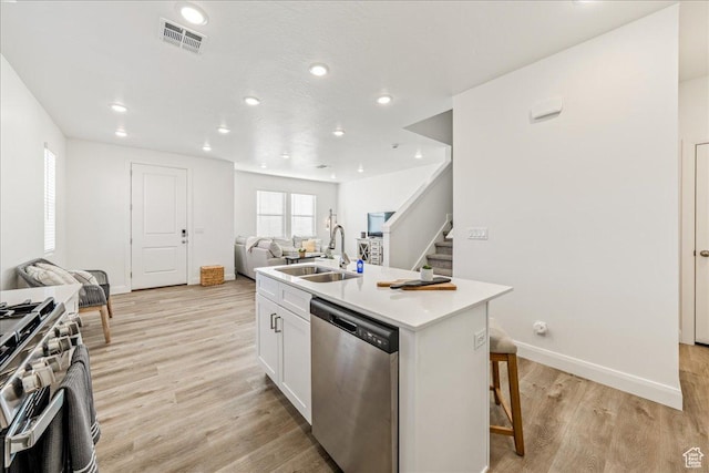 kitchen with light wood finished floors, visible vents, open floor plan, stainless steel appliances, and a sink