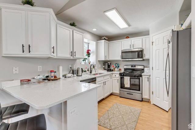 kitchen with light wood finished floors, a peninsula, a sink, appliances with stainless steel finishes, and white cabinetry