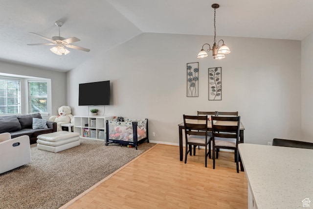 living room with ceiling fan with notable chandelier, vaulted ceiling, light wood-style floors, and baseboards