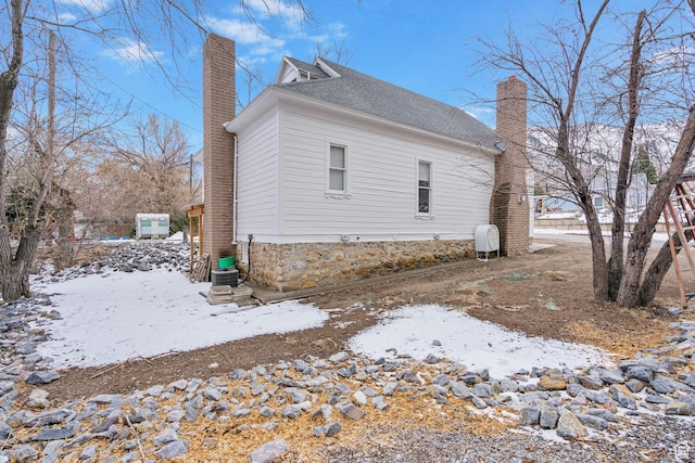 snow covered house with a chimney and a shingled roof