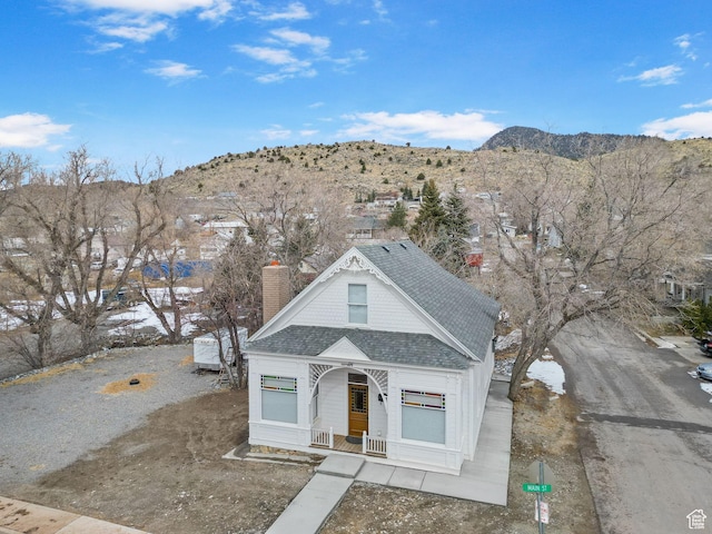 victorian house featuring a mountain view, roof with shingles, a porch, and a chimney