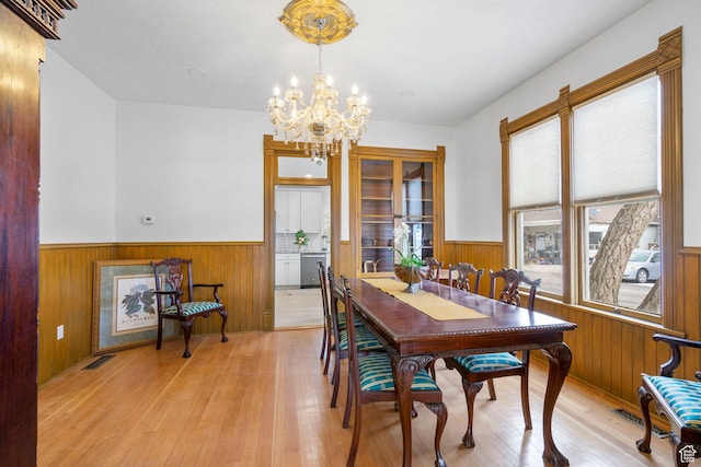 dining area featuring wooden walls, visible vents, a wainscoted wall, light wood-type flooring, and a chandelier