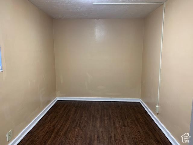 empty room with baseboards, a textured ceiling, and dark wood-style floors