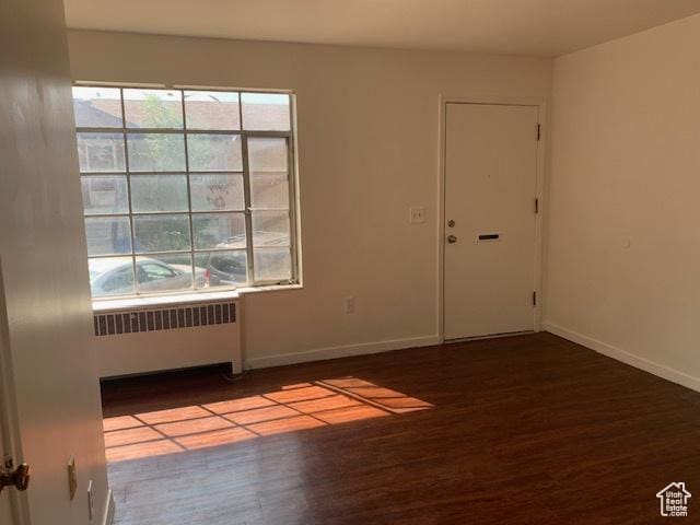 spare room with baseboards, radiator, and wood finished floors