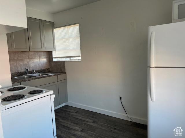 kitchen with a sink, backsplash, dark countertops, white appliances, and baseboards