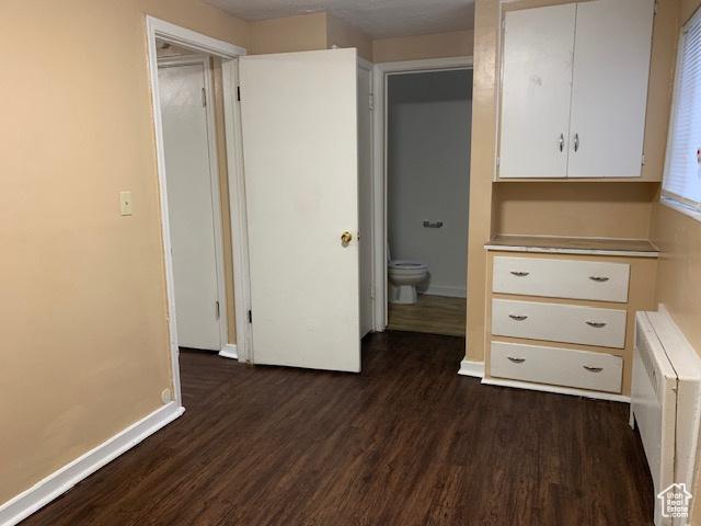 unfurnished bedroom featuring baseboards, radiator heating unit, and dark wood-type flooring