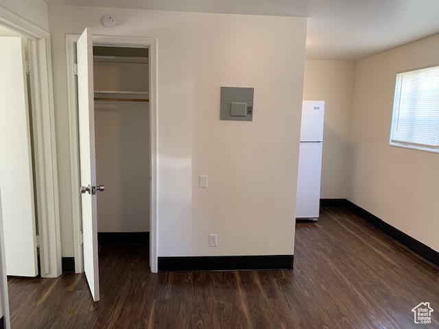 unfurnished bedroom featuring baseboards, freestanding refrigerator, and dark wood-type flooring