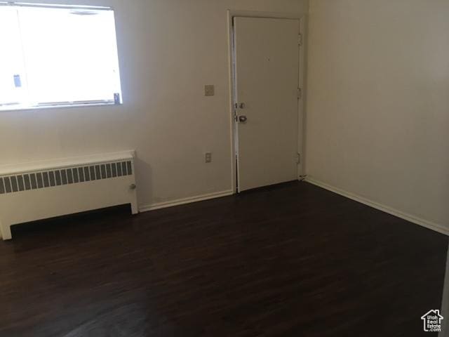 spare room with dark wood finished floors, radiator heating unit, and baseboards