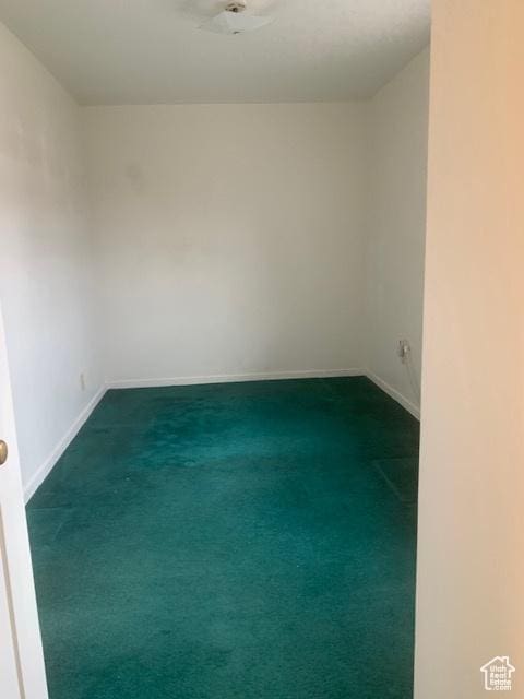 unfurnished room with baseboards and dark colored carpet
