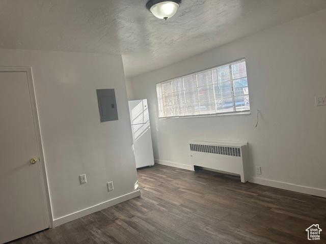 empty room with radiator, wood finished floors, baseboards, electric panel, and a textured ceiling