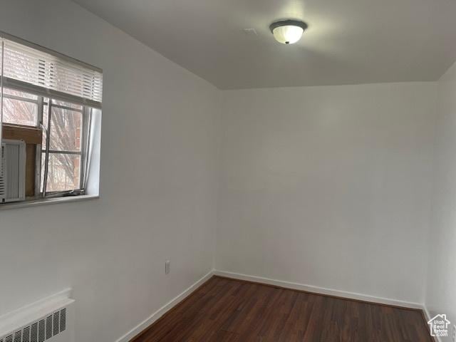 spare room with baseboards, radiator, and dark wood-type flooring