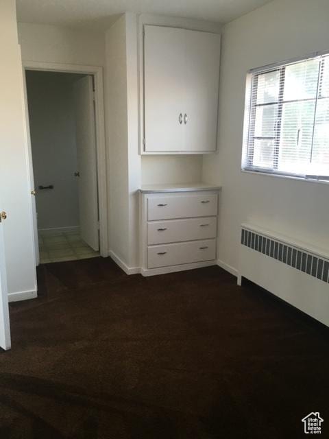 unfurnished bedroom with dark wood-type flooring, radiator heating unit, and baseboards
