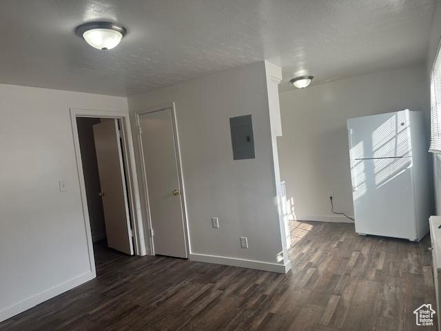 empty room featuring electric panel, dark wood-style floors, a textured ceiling, and baseboards