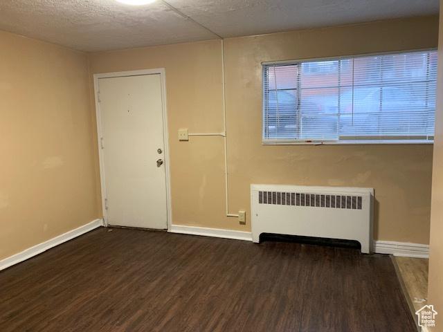 unfurnished room with baseboards, radiator, and wood finished floors