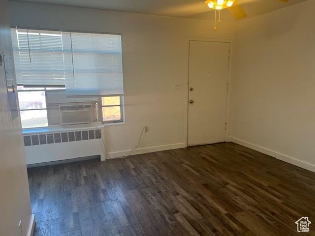 empty room featuring dark wood-style floors, cooling unit, radiator, and baseboards
