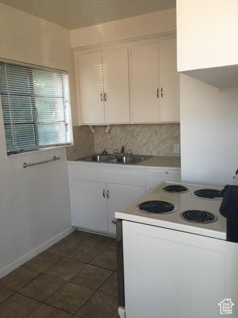 kitchen featuring electric range, a sink, white cabinetry, dark tile patterned floors, and backsplash