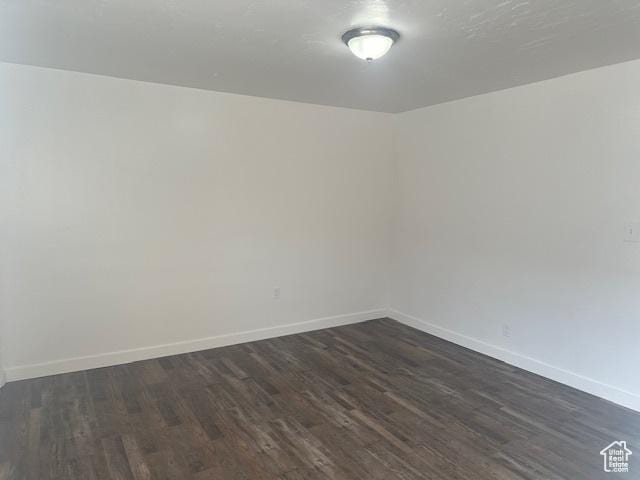 unfurnished room featuring baseboards and dark wood-style flooring