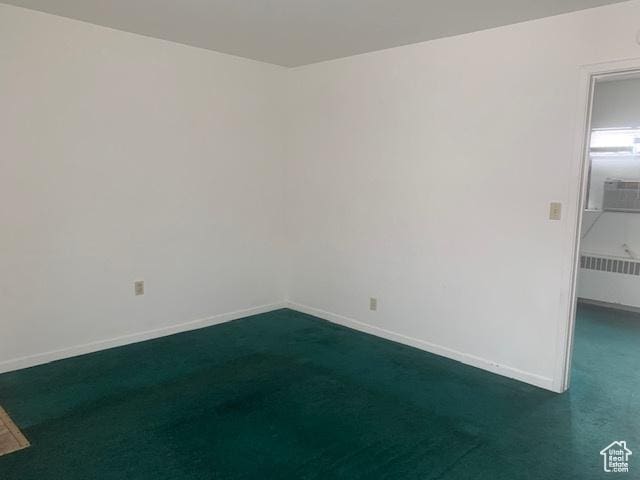 empty room with radiator heating unit, baseboards, and dark colored carpet