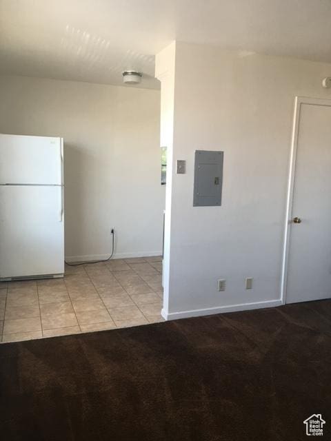 interior space with electric panel, freestanding refrigerator, light tile patterned flooring, baseboards, and light colored carpet