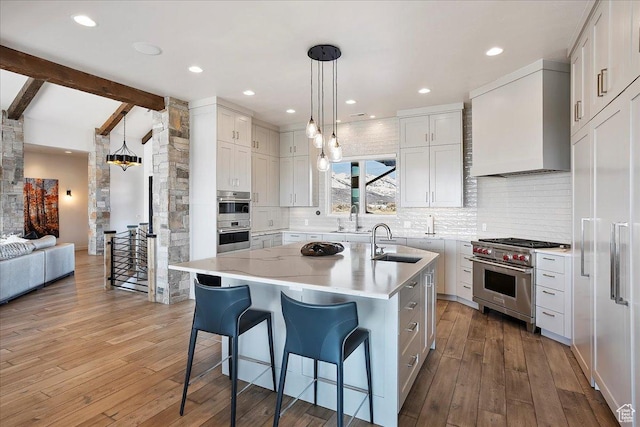 kitchen featuring a breakfast bar, custom range hood, a sink, appliances with stainless steel finishes, and light wood finished floors