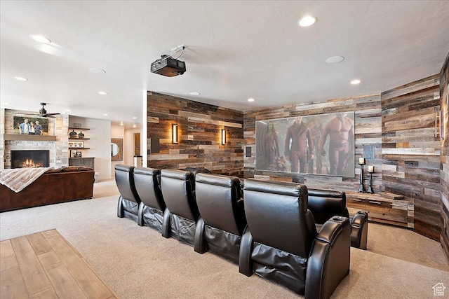 carpeted cinema with a stone fireplace, wooden walls, recessed lighting, and ceiling fan