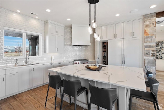 kitchen with a sink, tasteful backsplash, light wood-style floors, and wall chimney range hood