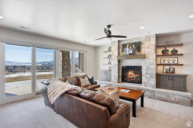 living room with visible vents, light carpet, a mountain view, a stone fireplace, and ceiling fan