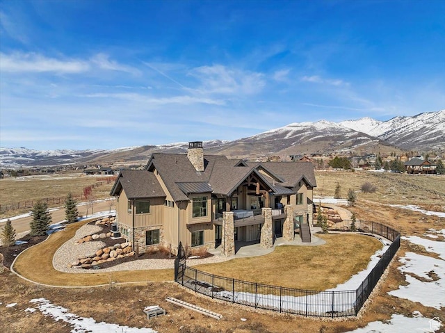 back of house with stone siding, a fenced backyard, a mountain view, board and batten siding, and a patio area