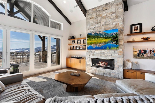 living area with wood finished floors, visible vents, high vaulted ceiling, a stone fireplace, and beamed ceiling
