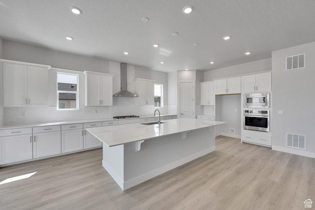 kitchen featuring wall chimney exhaust hood, stainless steel appliances, a sink, white cabinets, and recessed lighting