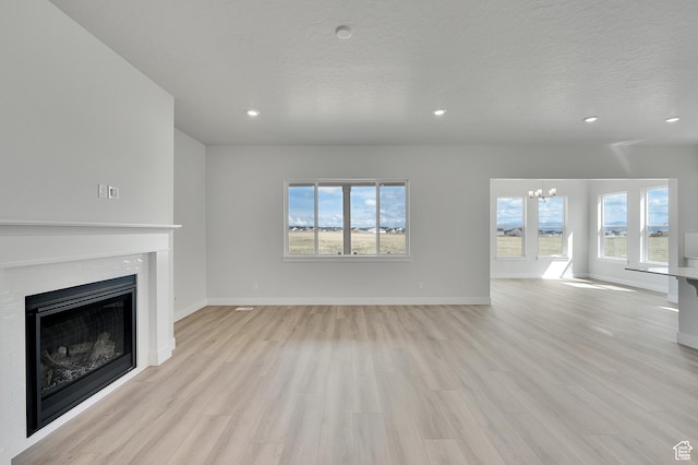 unfurnished living room with light wood-style floors, a chandelier, a fireplace, recessed lighting, and baseboards