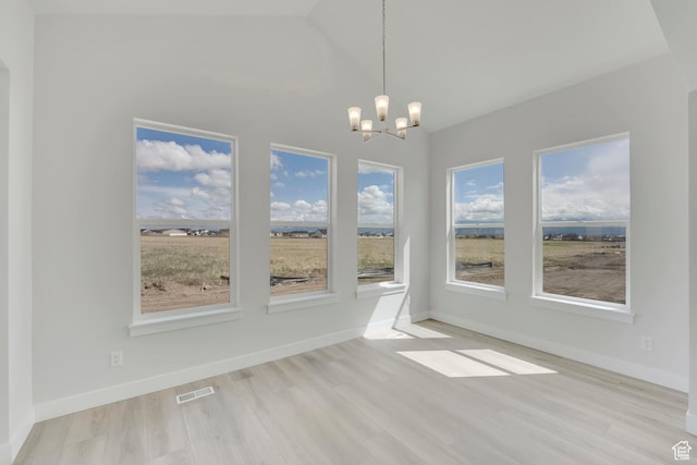 unfurnished dining area with a chandelier, plenty of natural light, light wood finished floors, lofted ceiling, and baseboards