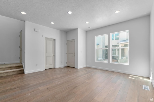 unfurnished living room featuring baseboards, light wood-type flooring, recessed lighting, and a textured ceiling