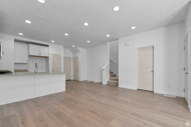 unfurnished living room with a textured ceiling, recessed lighting, stairway, and light wood-type flooring