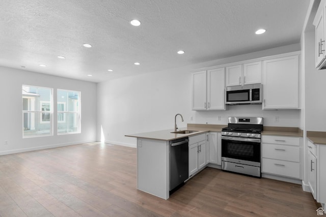 kitchen featuring white cabinetry, dark wood finished floors, a sink, a peninsula, and appliances with stainless steel finishes