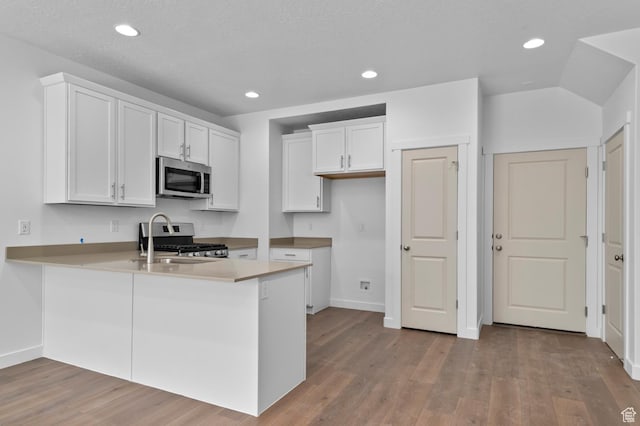 kitchen featuring wood finished floors, a peninsula, stainless steel appliances, white cabinets, and recessed lighting