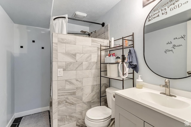 bathroom with baseboards, toilet, vanity, a tile shower, and a textured ceiling