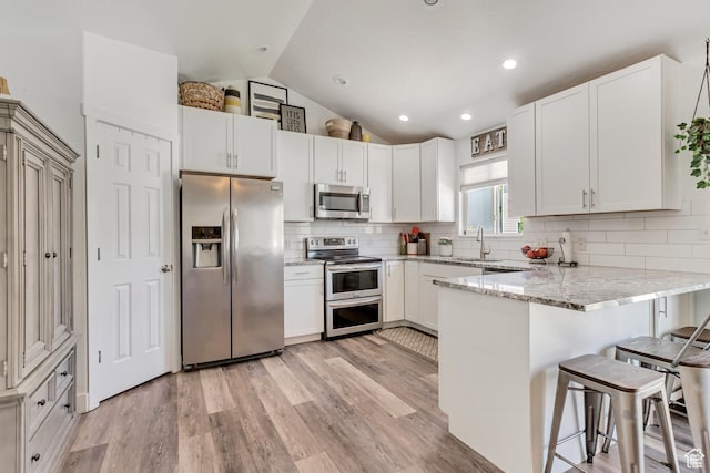 kitchen with vaulted ceiling, appliances with stainless steel finishes, a kitchen breakfast bar, a peninsula, and a sink