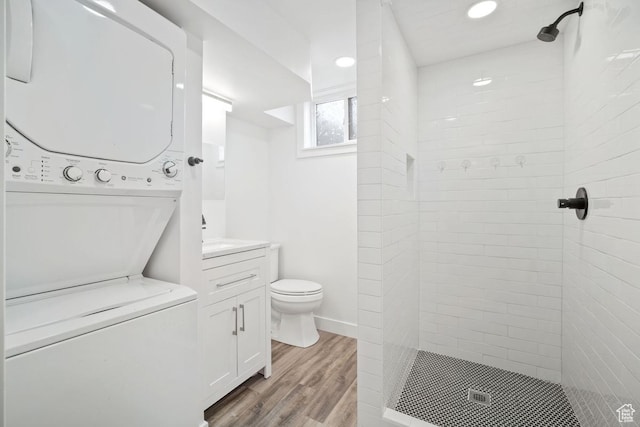 bathroom featuring vanity, wood finished floors, a shower stall, stacked washer and dryer, and toilet