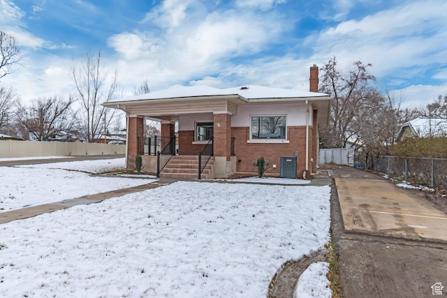 view of front of house featuring brick siding, fence, a chimney, and a porch