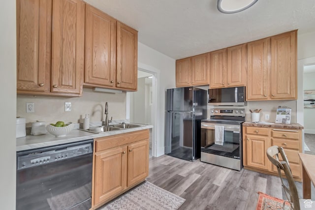 kitchen featuring light countertops, a sink, black appliances, and light wood-type flooring