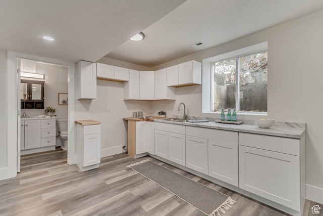 kitchen with baseboards, white cabinetry, light wood-style floors, and a sink